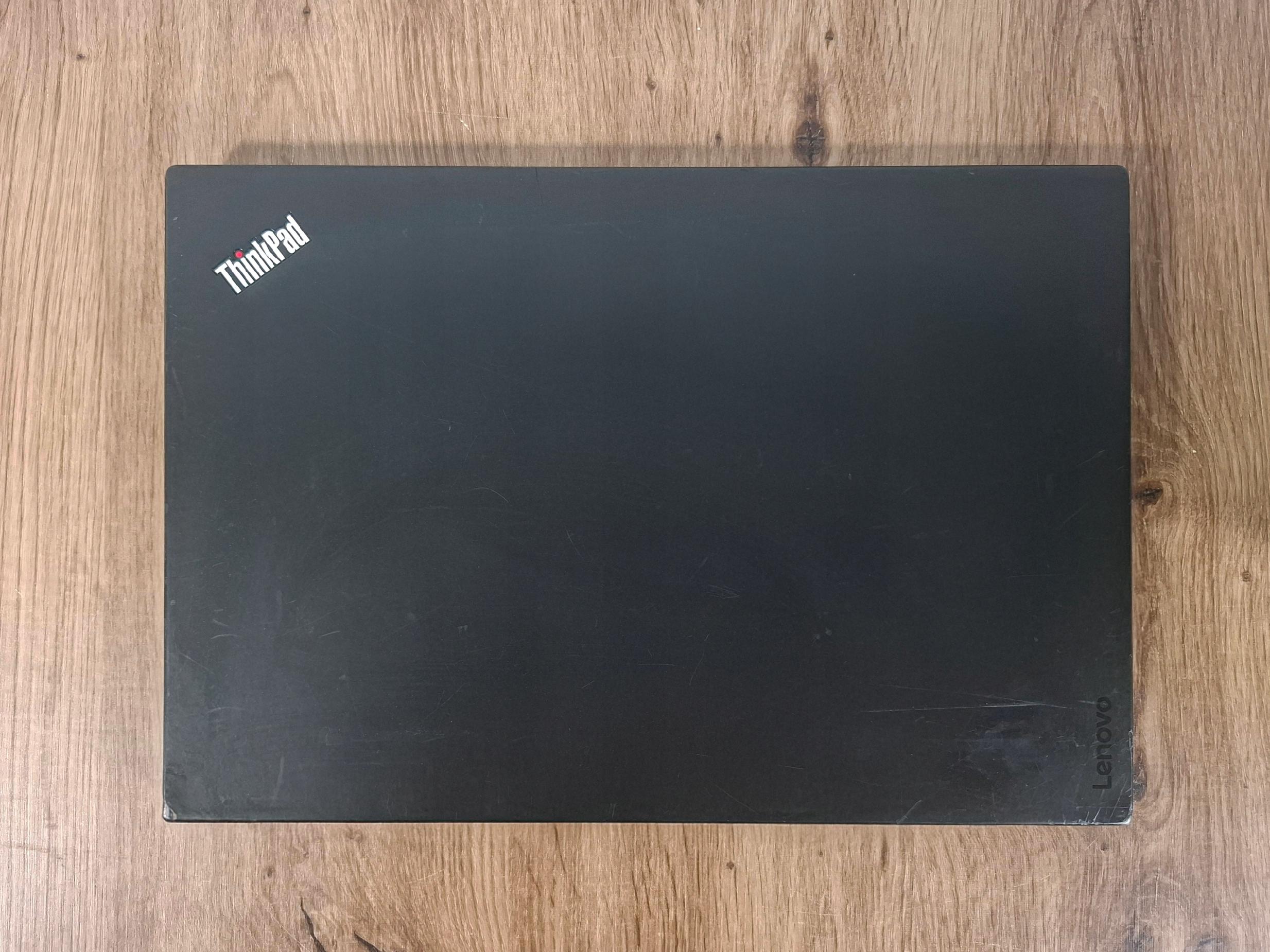 Zamknięta klapa laptopa ThinkPad z widocznym logo, obudowa z lekkimi śladami użytkowania, leży na drewnianym blacie.