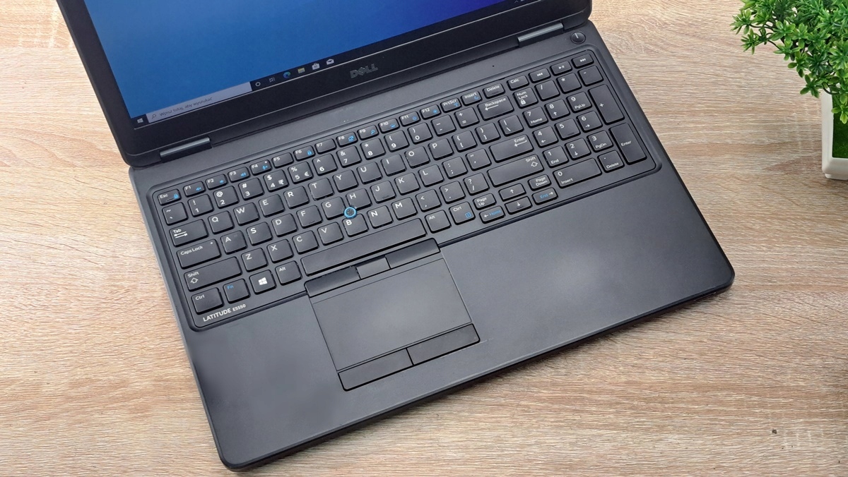 Laptop Dell Latitude E5550 otwarty, widok z góry na klawiaturę i touchpad, ekran włączony w tle rozmyty