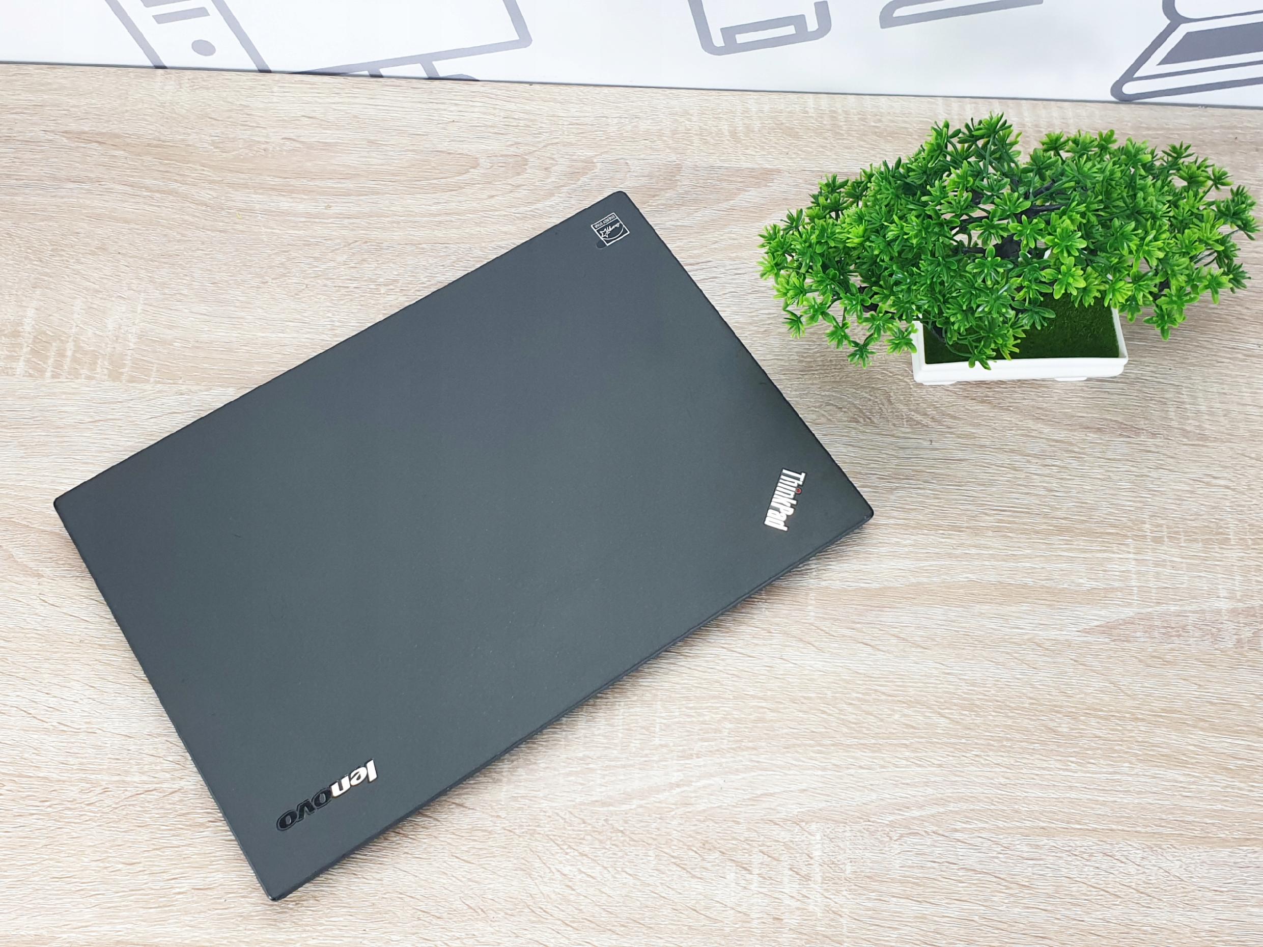 Zamknięty laptop Lenovo ThinkPad T450 z logo na pokrywie, widok z góry na drewnianym biurku obok doniczki z rośliną.