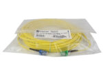 Zwinięty żółty kabel światłowodowy w foliowym opakowaniu, widoczne złącza LC i LC/APC oraz naklejka z opisem produktu.