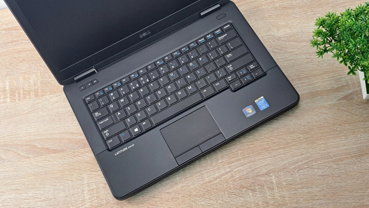 Otwarty laptop Dell Latitude widziany z góry pod kątem, widoczna klawiatura i touchpad na tle drewnianego blatu.