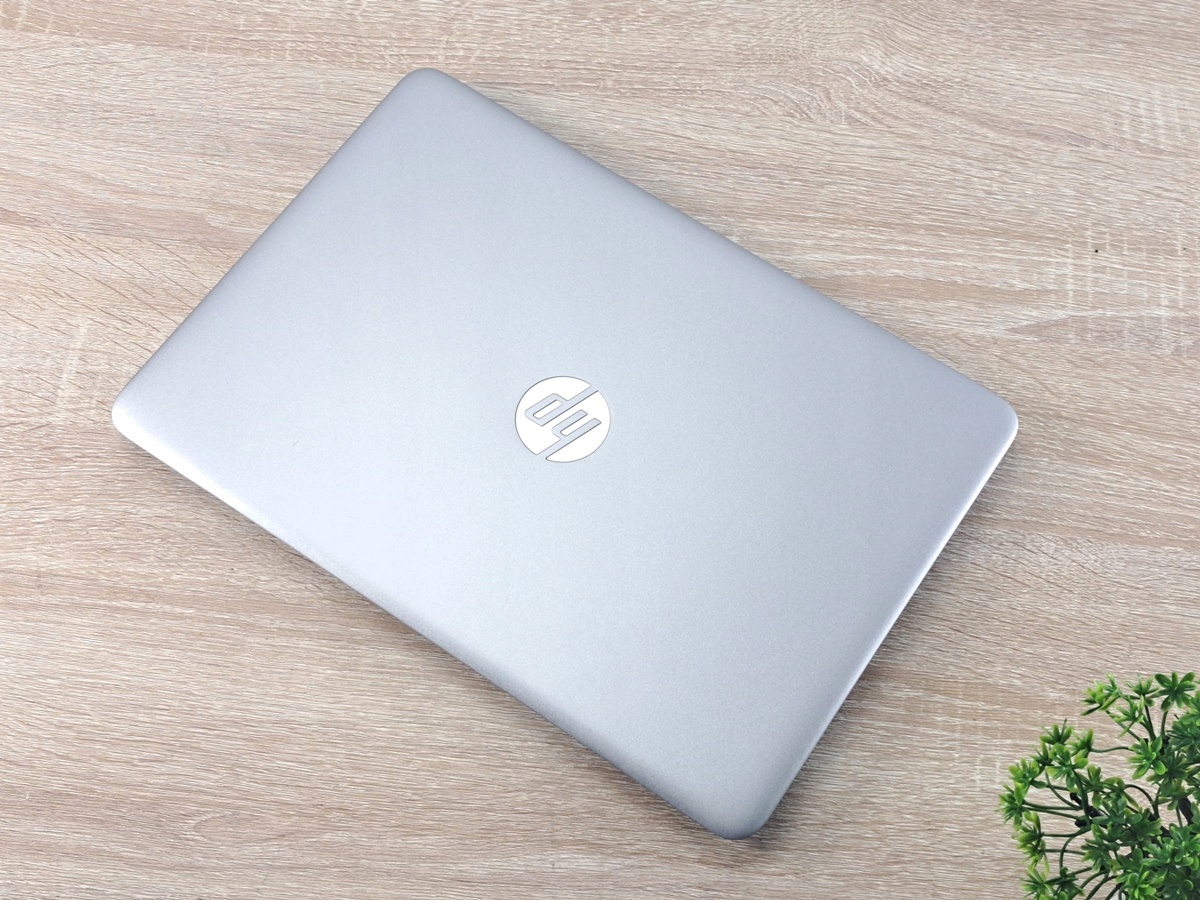 Zamknięty laptop HP Elitebook z logo na pokrywie, widok z góry na drewnianym blacie obok rośliny.