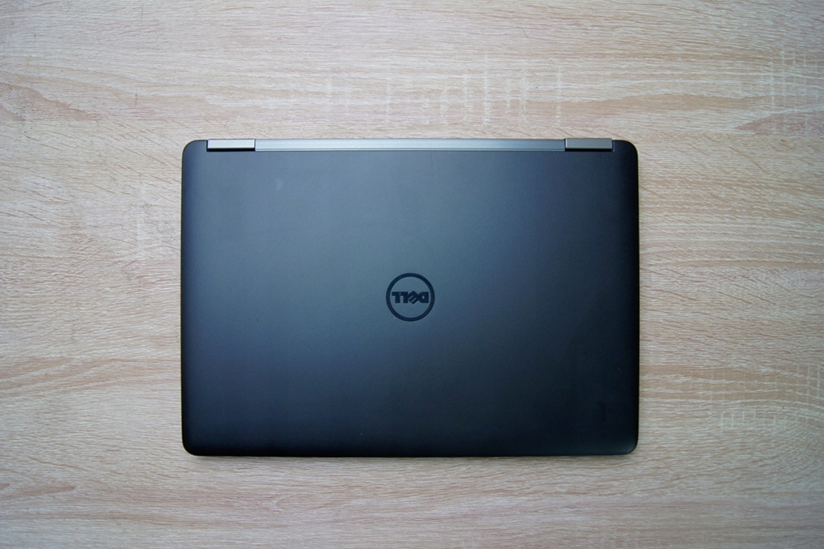Zamknięty laptop Dell widziany od tyłu z logo na klapie, obudowa czarna z lekkimi śladami użytkowania, na drewnianym blacie.