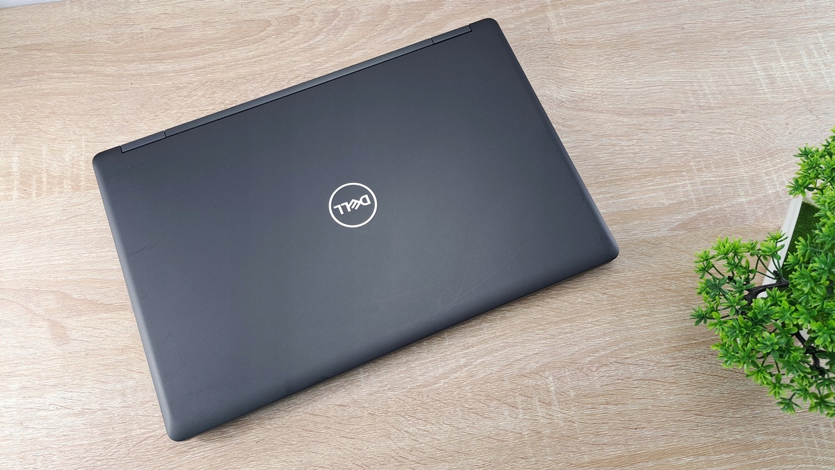 Zamknięty laptop Dell z logo na pokrywie, widok z góry pod kątem, obok roślina na biurku.