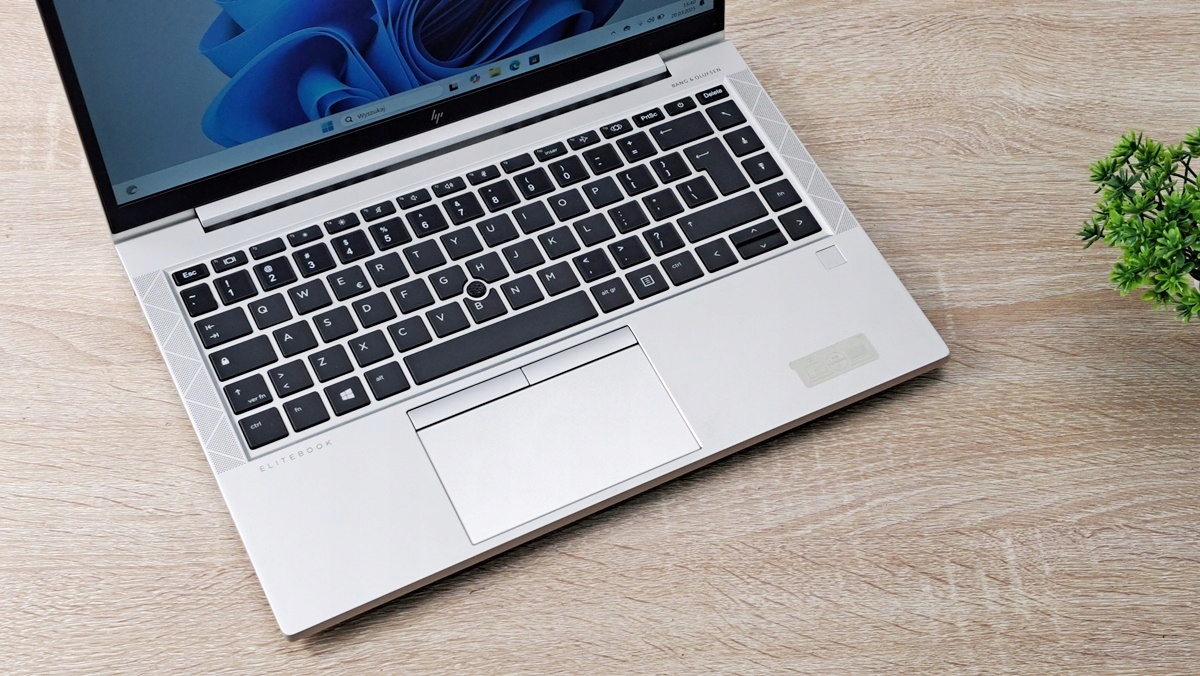 Laptop HP EliteBook 845 G7 widziany z góry pod kątem, otwarty, z widoczną klawiaturą i touchpadem na drewnianym blacie.