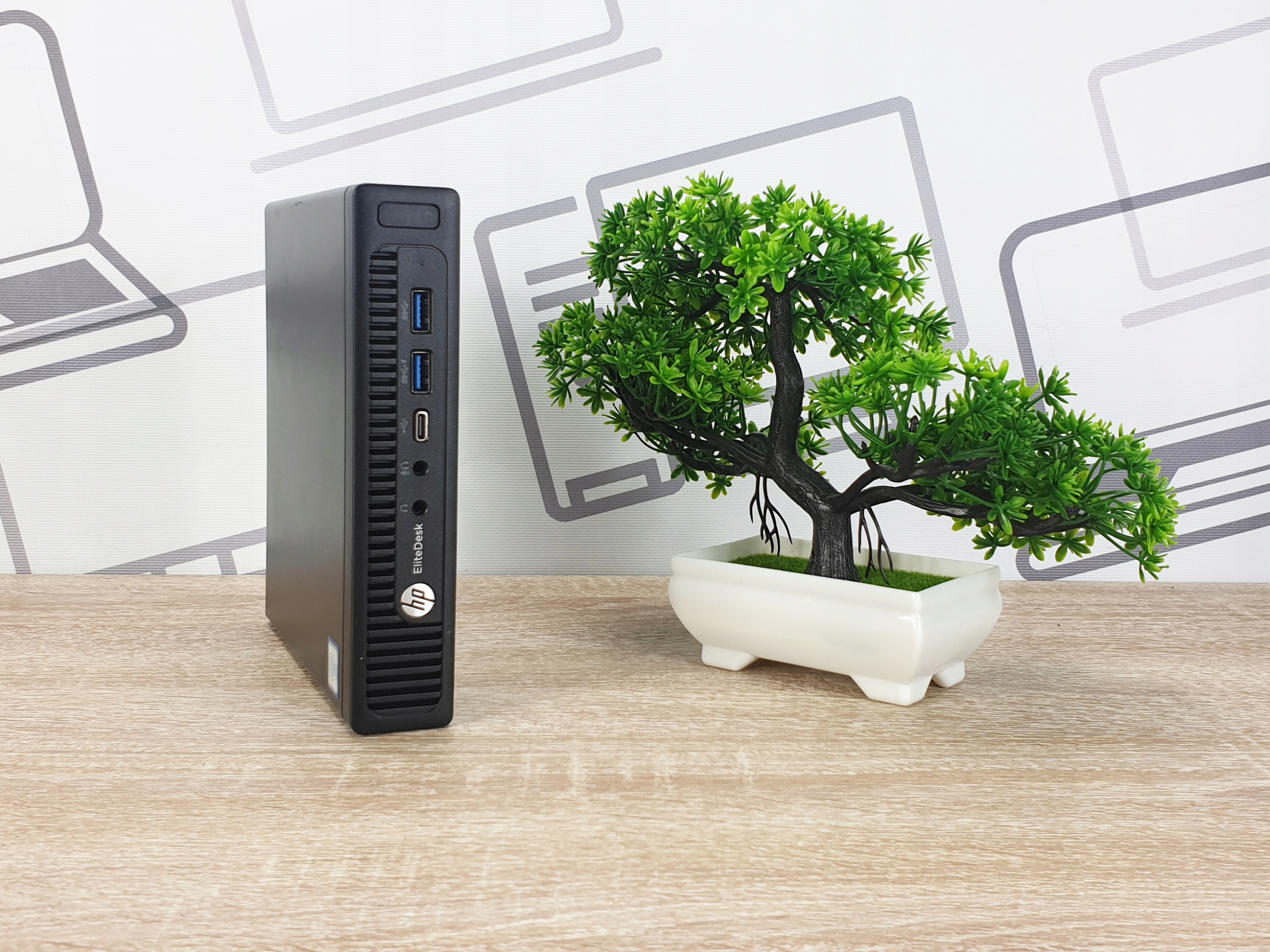Komputer HP EliteDesk 800 G2 Tiny stojący na biurku obok sztucznej bonsai, widoczny przedni panel z portami USB.