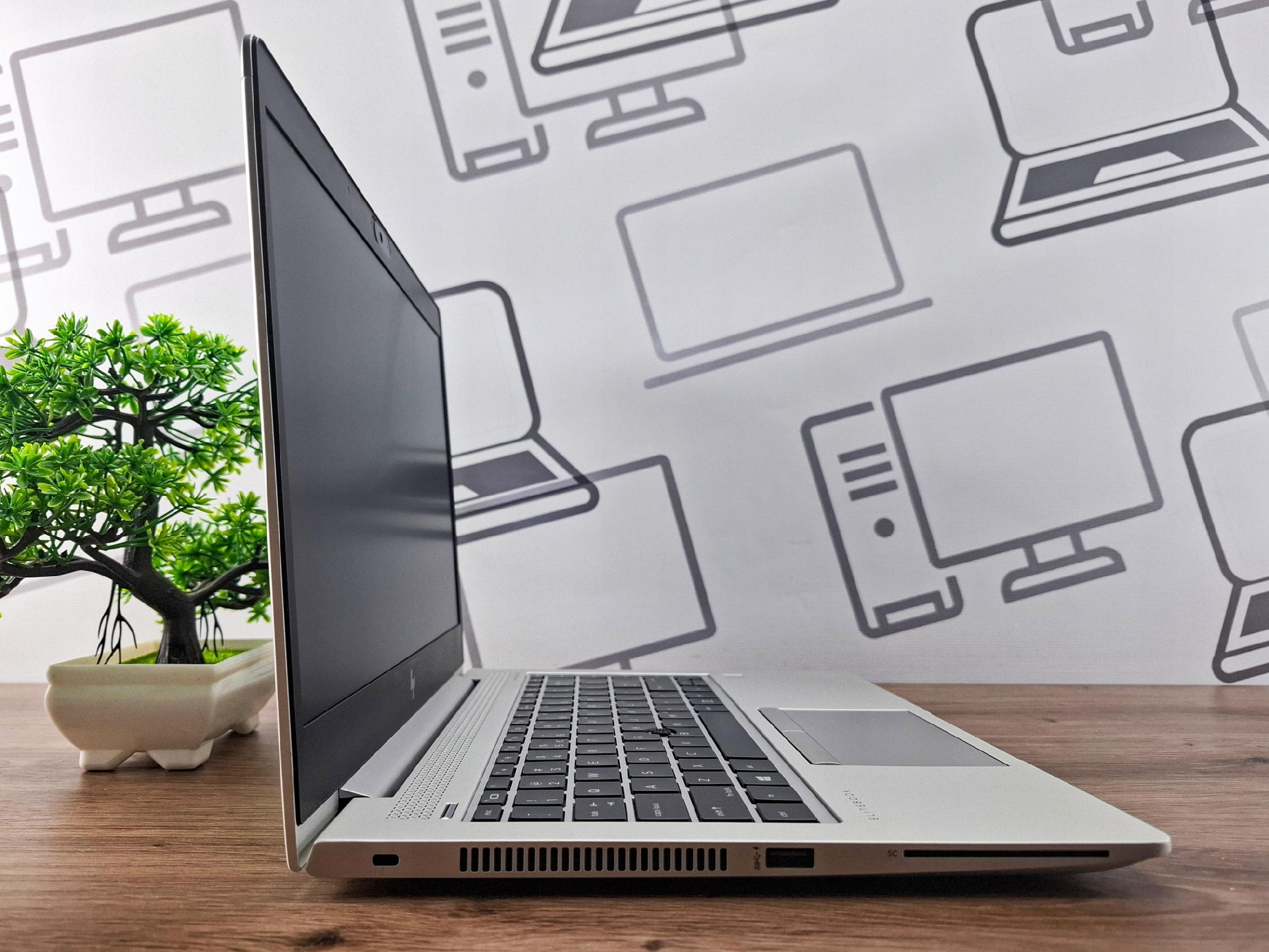 Laptop HP EliteBook otwarty pod kątem z boku, widok na profil klawiatury i wyłączony ekran, obok bonsai na biurku