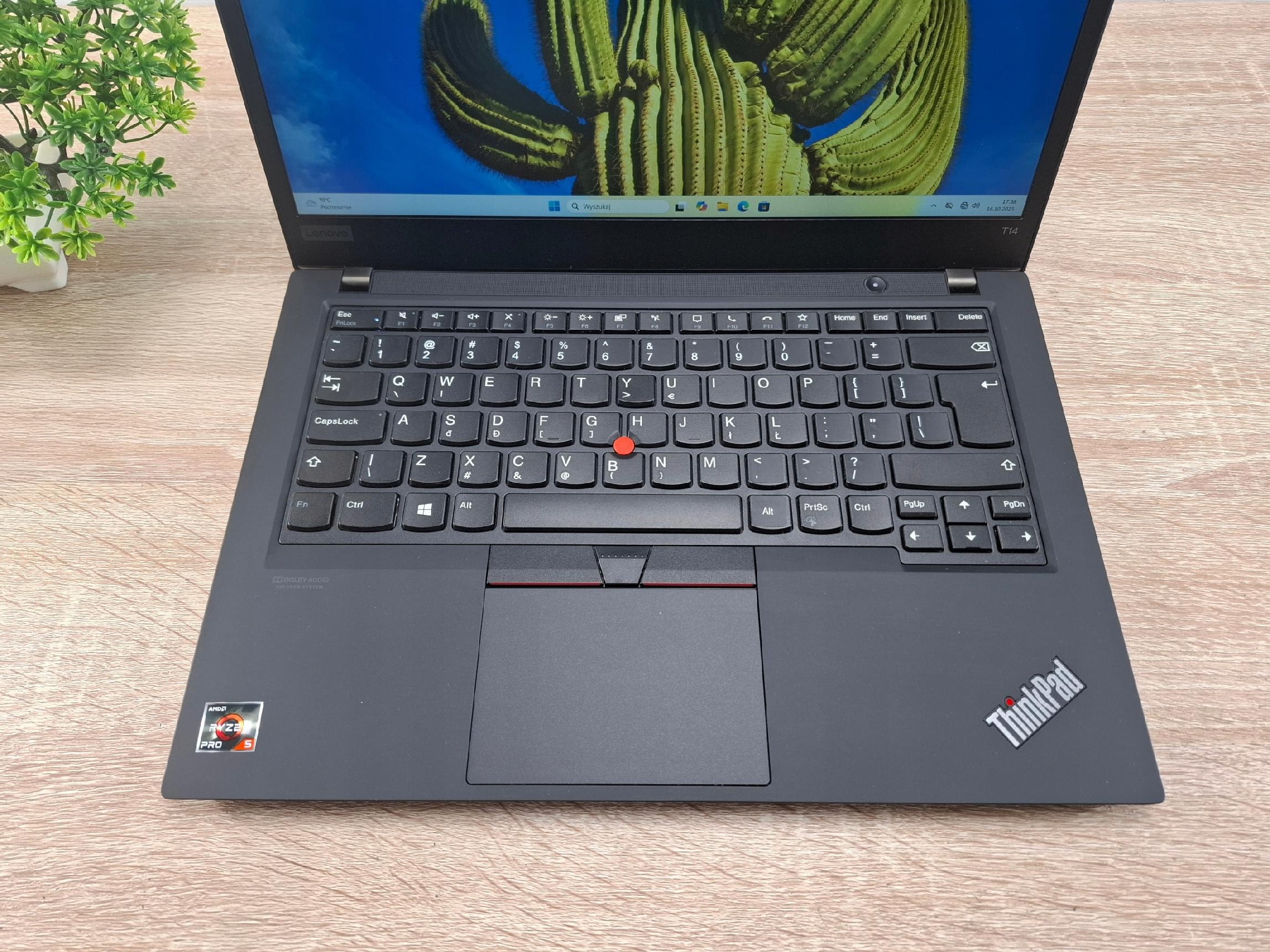 Otwarty laptop Lenovo ThinkPad T14 pod kątem z góry, widoczna klawiatura z czerwonym trackpointem i włączony ekran z tapetą.