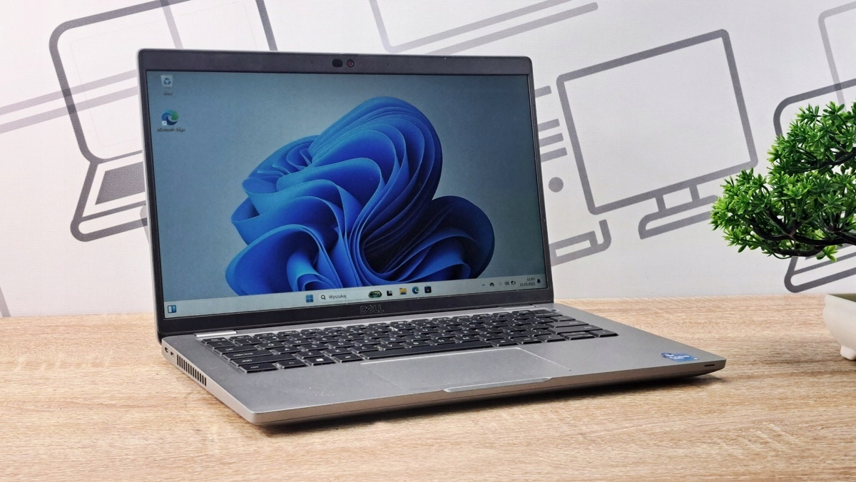 Otwarty laptop Dell Latitude ustawiony pod kątem, ekran włączony z pulpitem Windows, obudowa w kolorze srebrnym