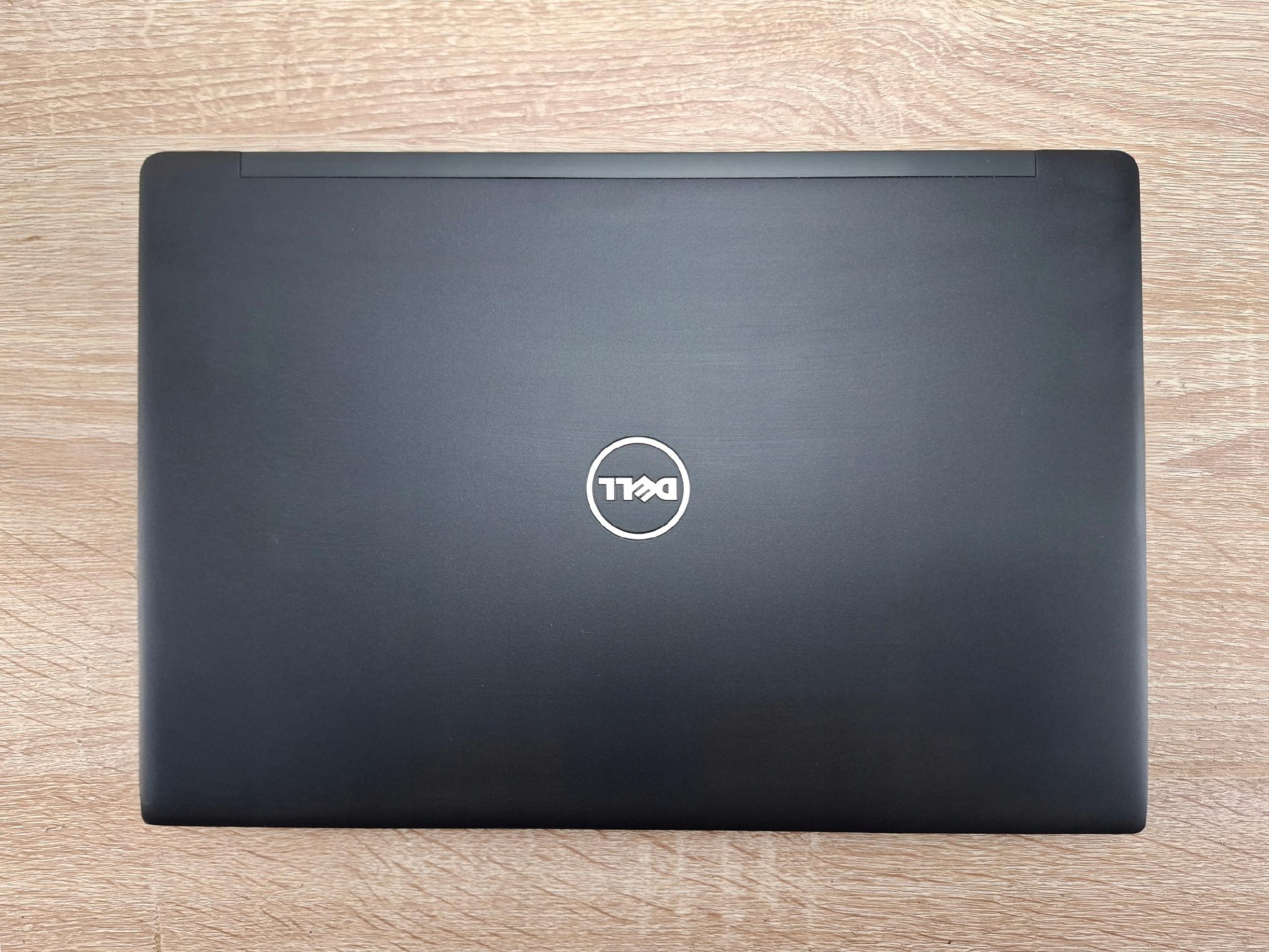 Zamknięty laptop Dell widziany od góry z logo na środku pokrywy, leżący na drewnianym blacie.
