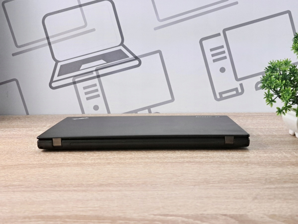 Zamknięty laptop Lenovo ThinkPad X250 widziany z boku, ukazujący smukłą, czarną obudowę na drewnianym blacie.