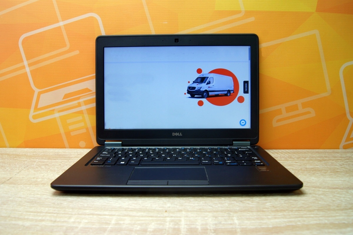 Otwarty laptop Dell E7250 od przodu, na ekranie ikona ostrzegawcza z pojazdem, obudowa z widocznymi śladami użytkowania.