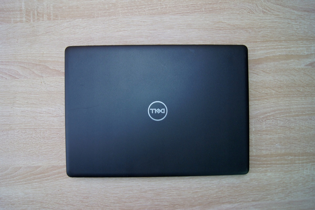 Zamknięty laptop Dell Latitude widziany od góry, czarna klapa z logo Dell na środku, na drewnianym blacie.