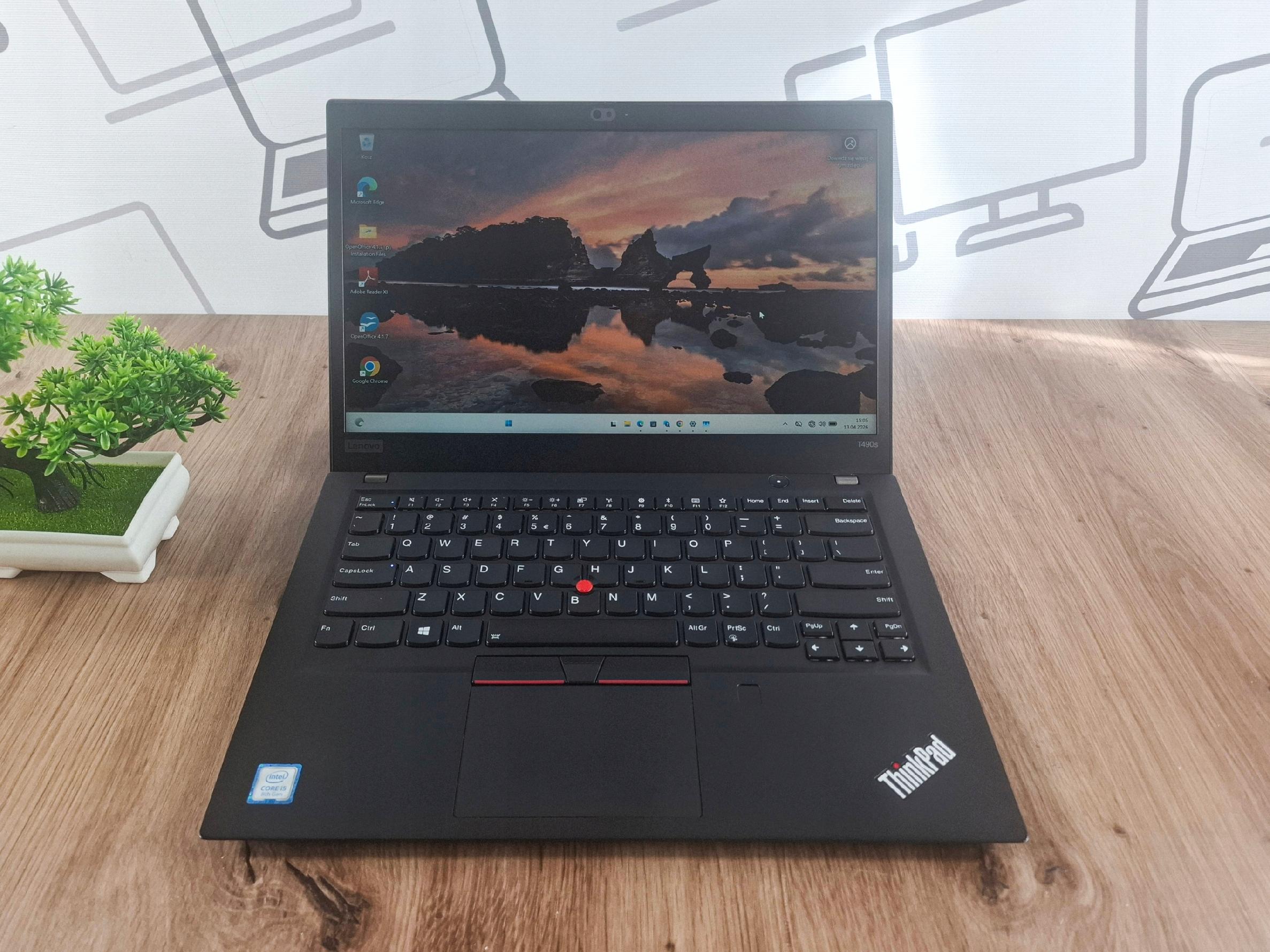 Otwarty laptop Lenovo ThinkPad T490s pod kątem z przodu, ekran włączony z widokiem górskiego krajobrazu.