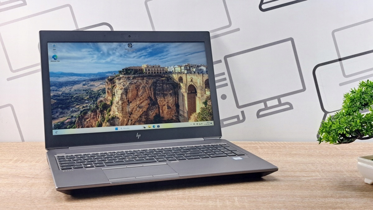 Otwarty laptop HP ZBook pod kątem z boku, na ekranie widoczny górski krajobraz z mostem, klawiatura z podświetleniem widoczna z profilu.