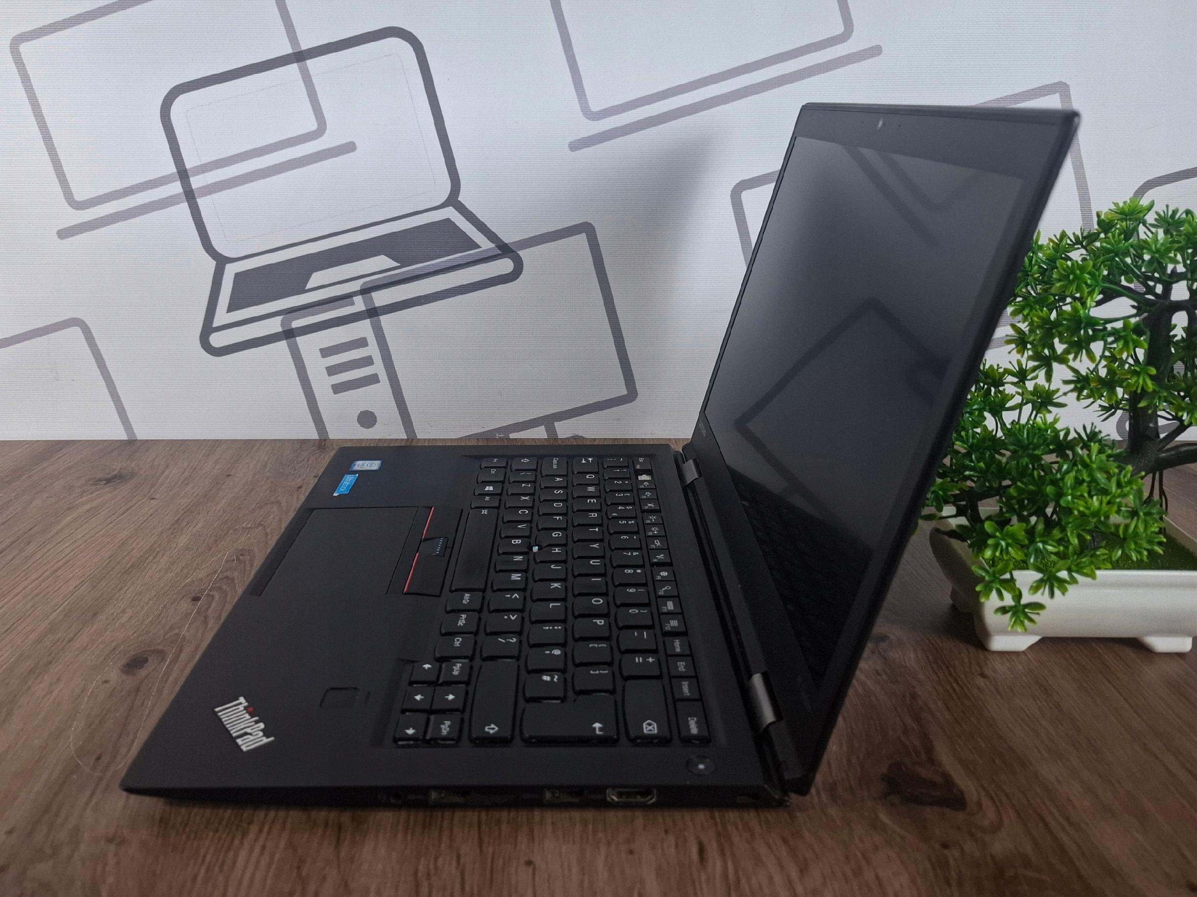 Otwarty laptop Lenovo ThinkPad X1 Carbon widziany z boku pod kątem, ekran wygaszony, widoczna klawiatura i logo ThinkPad.