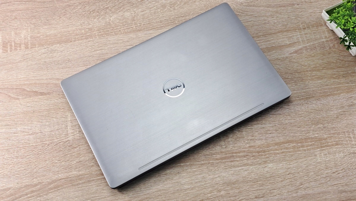 Zamknięty laptop Dell z logo na pokrywie, widok od góry pod kątem, obudowa w kolorze srebrnym z lekkimi śladami użytkowania.