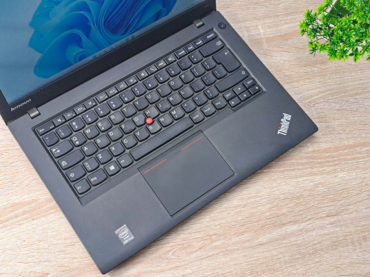 Otwarty laptop Lenovo ThinkPad T440 z góry, widoczna klawiatura z czerwonym trackpointem i touchpad na tle drewnianego blatu.