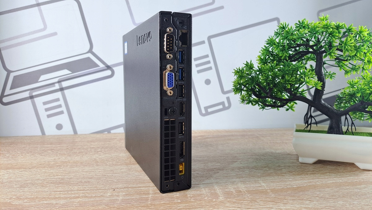Boczny panel komputera Lenovo ThinkCentre M920Q Tiny z portami VGA, USB i złączem sieciowym, obudowa stojąca na biurku.