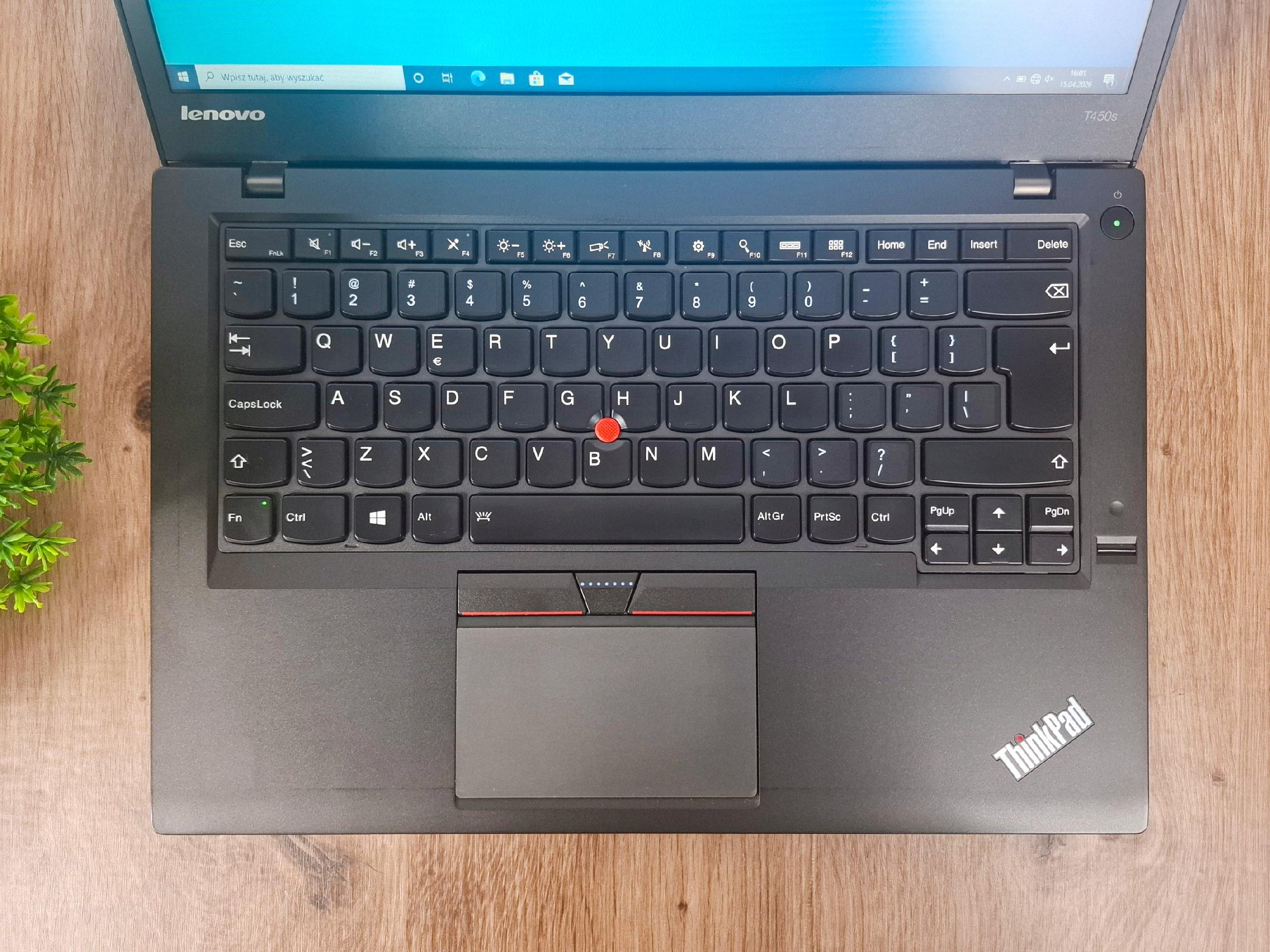Otwarty laptop Lenovo ThinkPad T450s widziany z góry, klawiatura z czerwonym trackpointem i ekran z logo Lenovo w tle.