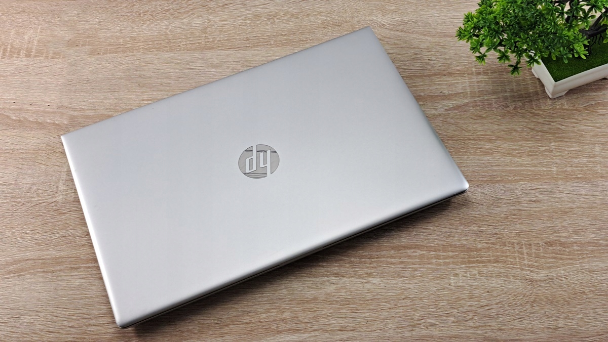 Zamknięty srebrny laptop HP z widocznym logo na pokrywie, ustawiony pod kątem na drewnianym blacie.