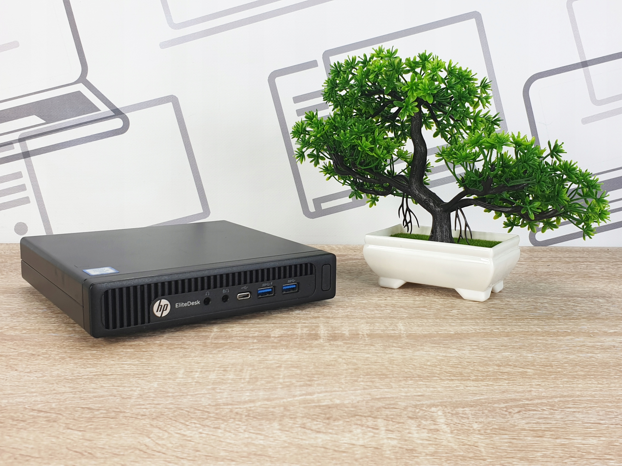 Mały komputer HP EliteDesk 800 G2 Tiny widziany z przodu na biurku, obok dekoracyjne drzewko bonsai.
