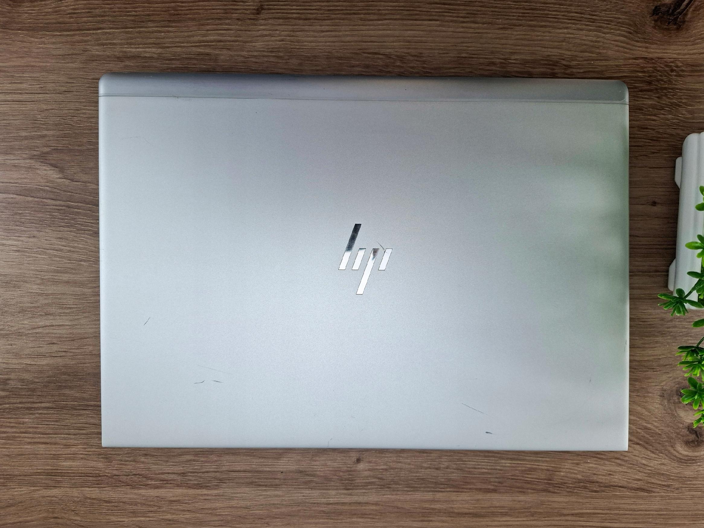 Zamknięta srebrna klapa laptopa HP EliteBook z logo pośrodku, widoczne drobne smugi i zabrudzenia na obudowie.