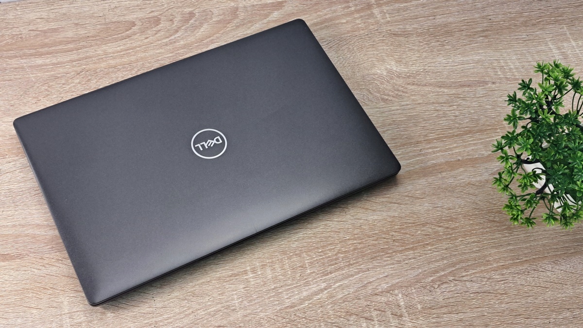 Zamknięty laptop Dell Latitude z logo na pokrywie, widok z góry pod kątem, obok mała doniczka z rośliną.