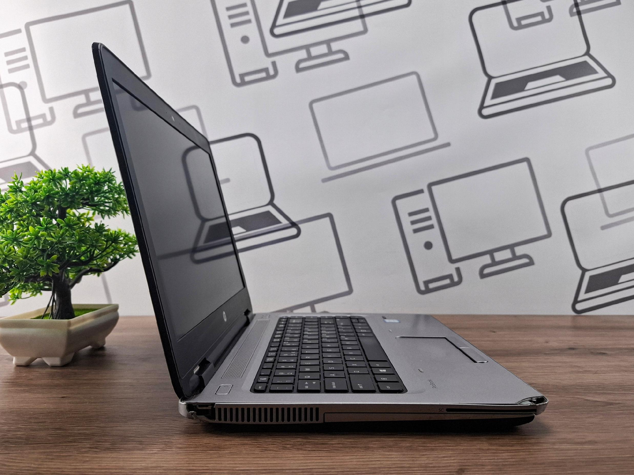Laptop HP ProBook otwarty pod kątem z boku, ekran wyłączony, na biurku obok bonsai.