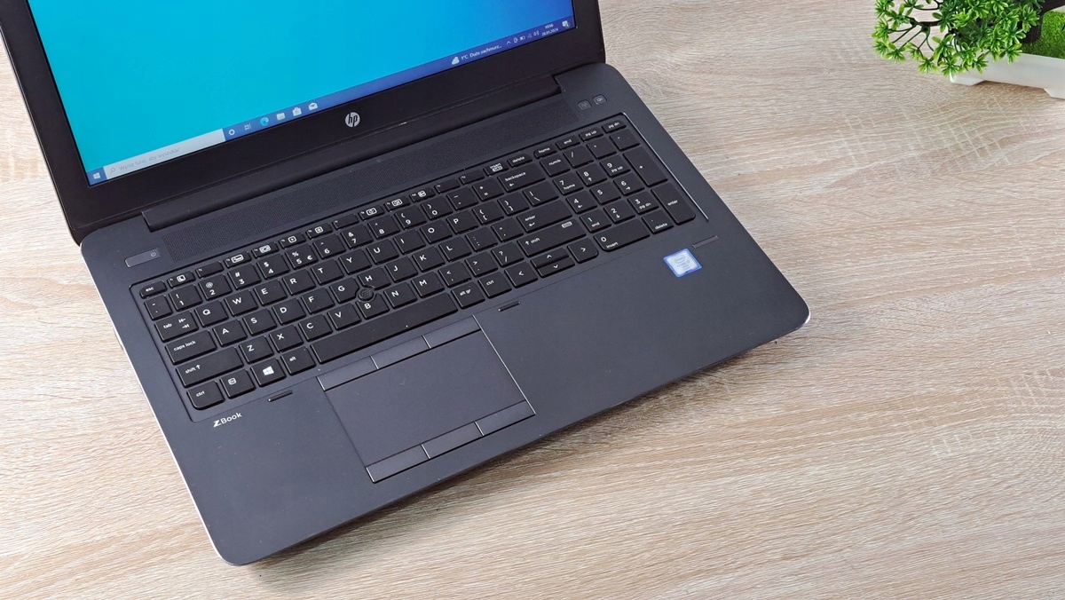 Laptop HP ZBook 15 G3 otwarty pod kątem z boku, widoczna klawiatura, touchpad i włączony ekran z zielonym tłem.