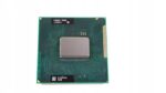 Procesor Intel z widoczną metalową puszką i zieloną płytką ze złotymi pinami PGA na spodzie.