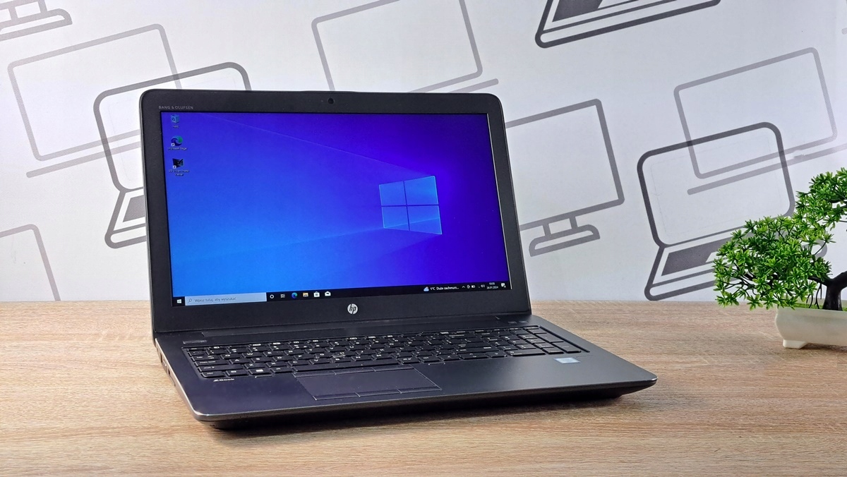 Otwarty laptop HP ZBook pod kątem z boku, ekran włączony z pulpitem Windows 10 w kolorze niebieskim.