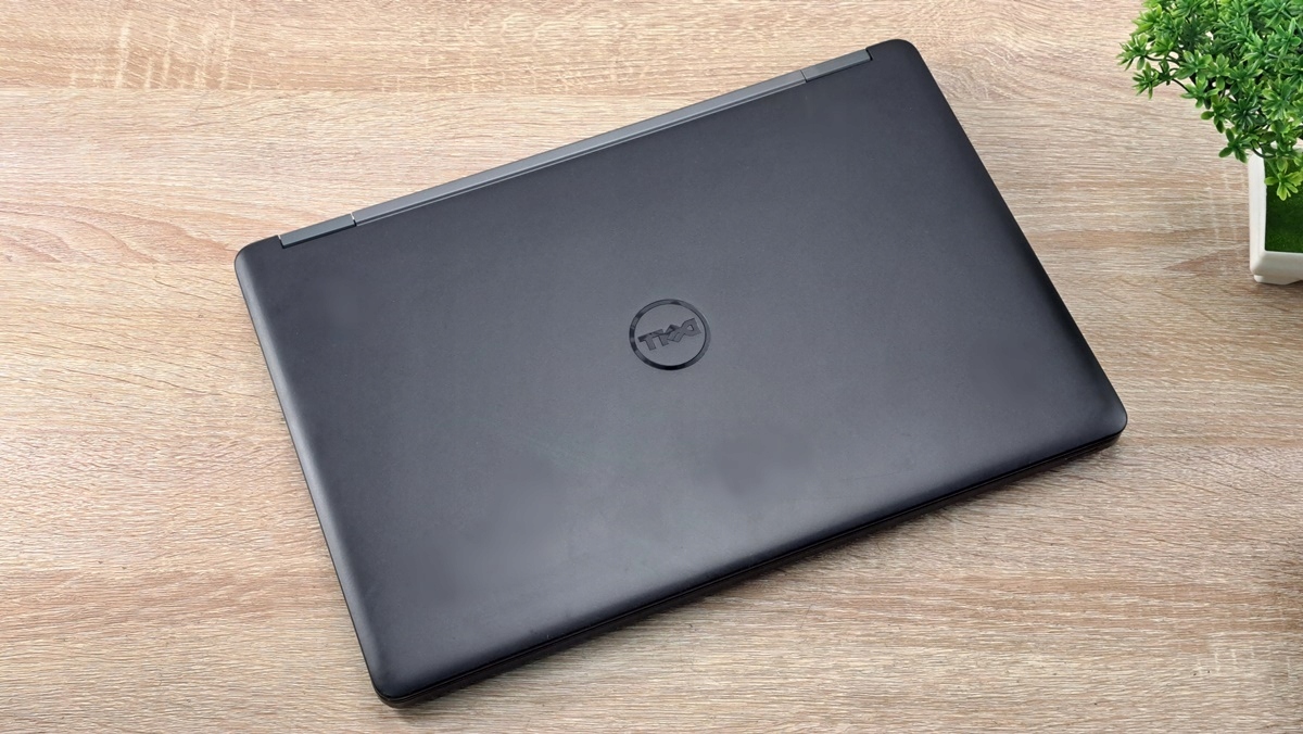 Zamknięty laptop Dell Latitude E5550 w czarnej obudowie, widok z góry na blacie z rośliną w tle.
