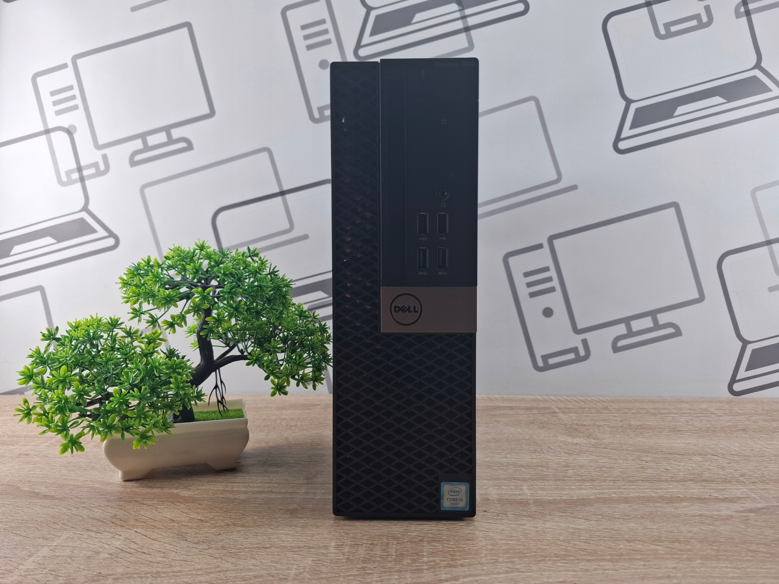Komputer Dell OptiPlex SFF ustawiony pionowo, widok przedni obudowy z logo, bez widocznych portów z tej strony.