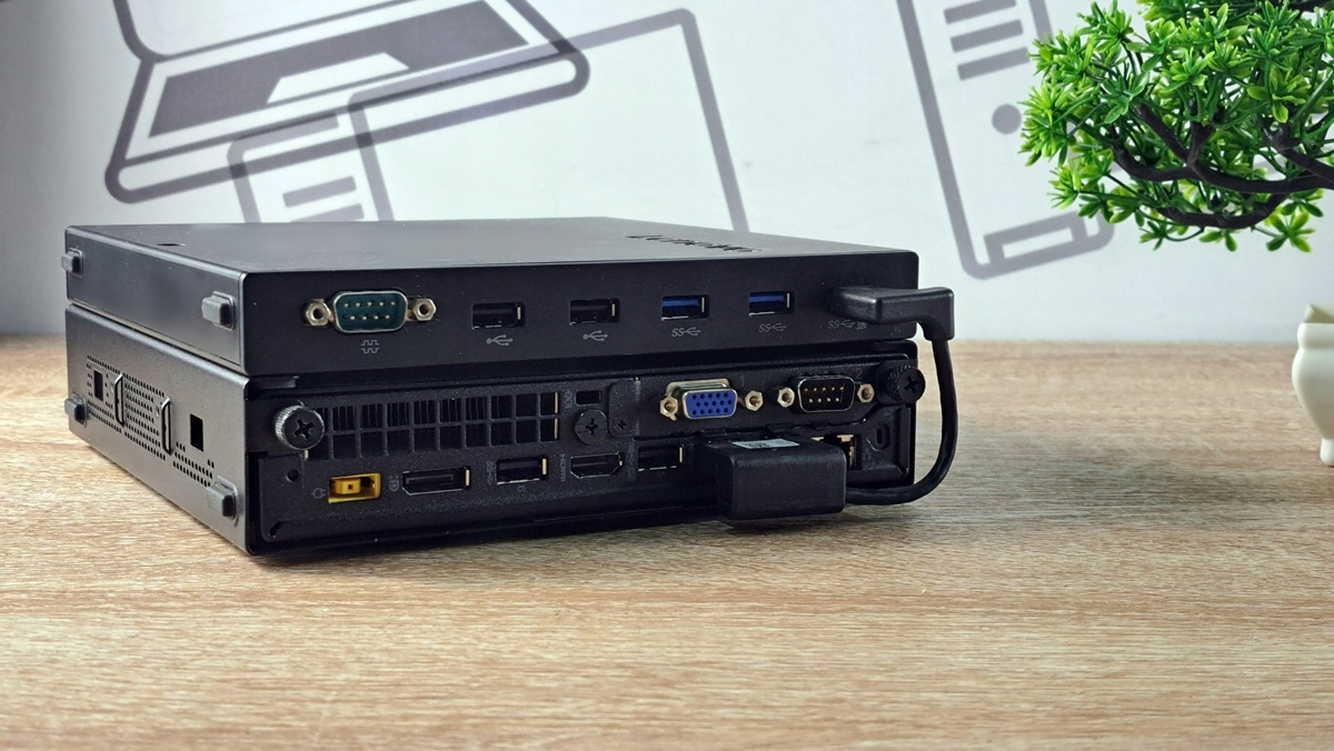 Mały komputer Lenovo ThinkCentre Tiny pod kątem z tyłu, widoczne porty USB, DisplayPort i VGA oraz podłączony kabel.