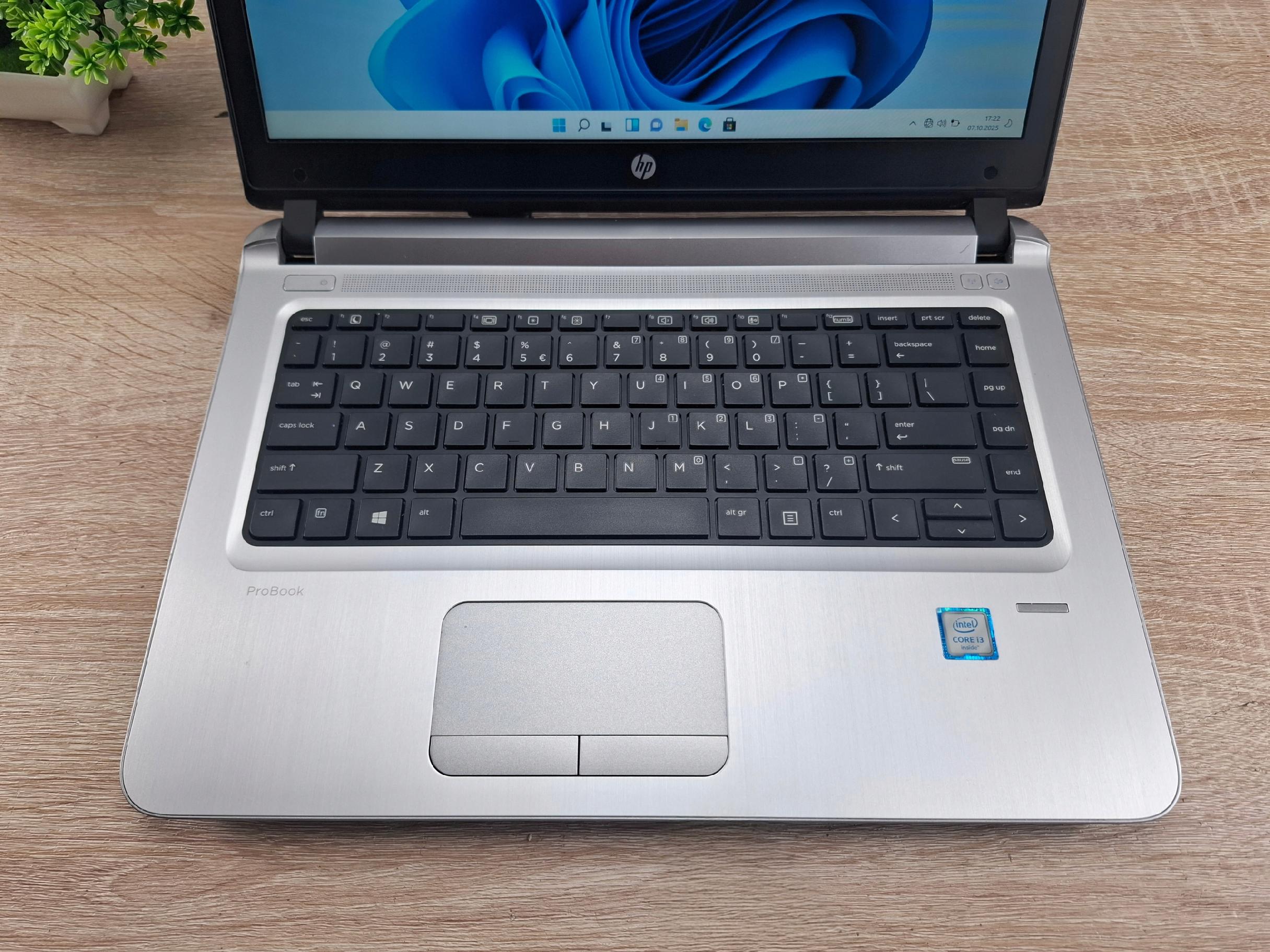 Otwarty laptop HP ProBook widziany z góry, klawiatura i touchpad w srebrnej obudowie, ekran włączony na blacie z drewnianym wzorem.