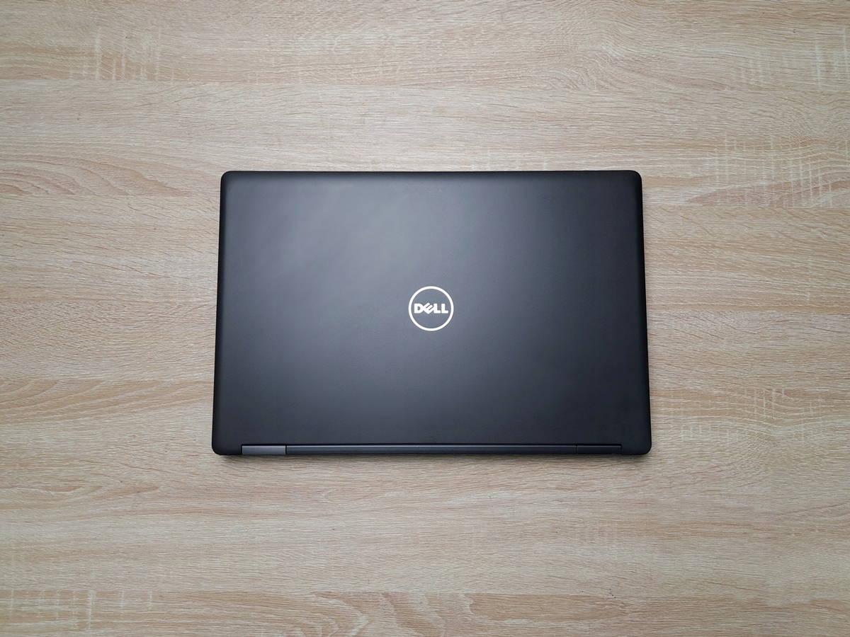 Zamknięty laptop Dell z logo na pokrywie, widok z góry na czarną obudowę leżącą na drewnianym blacie.