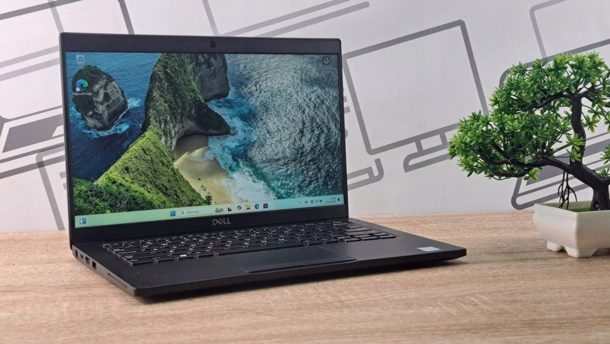 Otwarty laptop Dell Latitude ustawiony pod kątem na biurku, ekran włączony z widokiem górskiego krajobrazu.