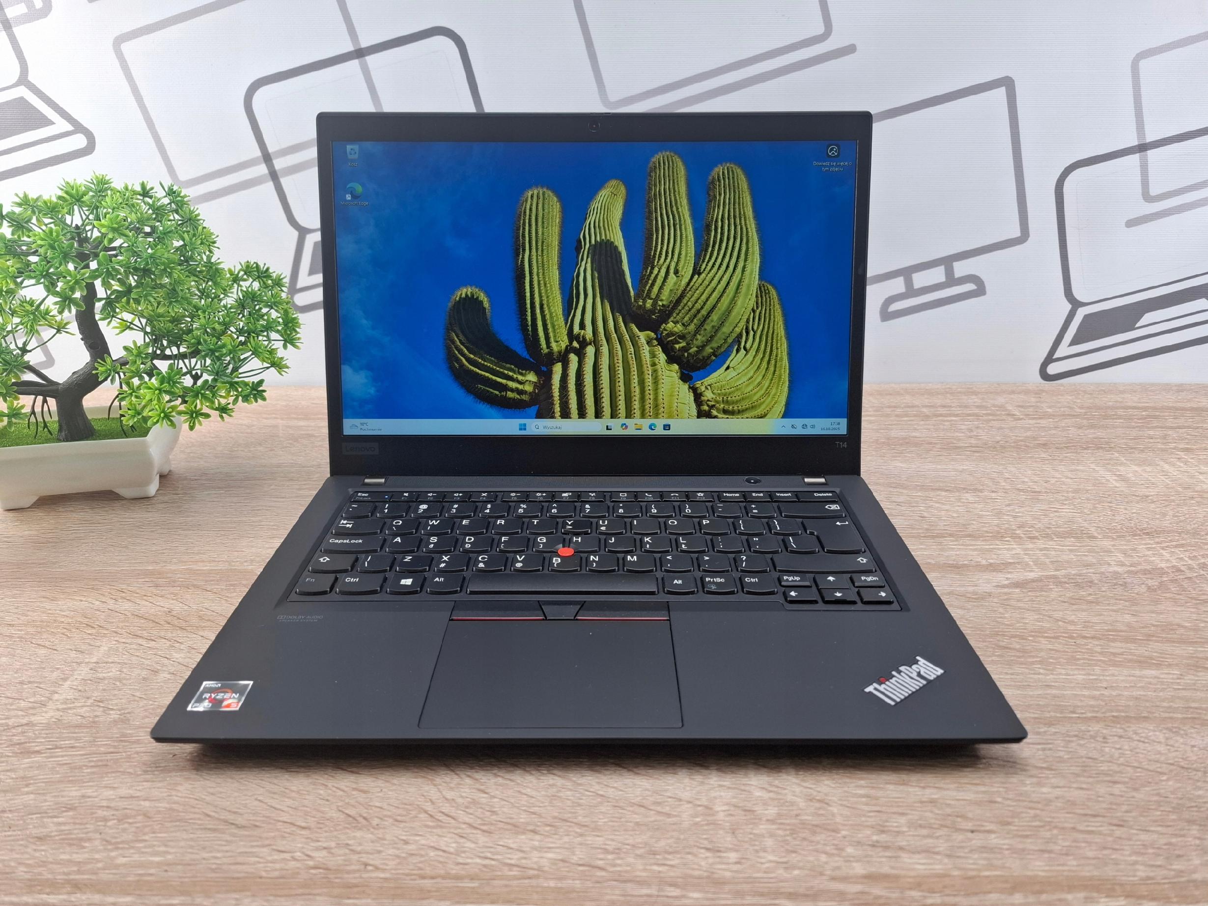 Otwarty laptop Lenovo ThinkPad T14 na biurku, ekran włączony z grafiką kaktusów, widoczna klawiatura z czerwonym akcentem TrackPointa.