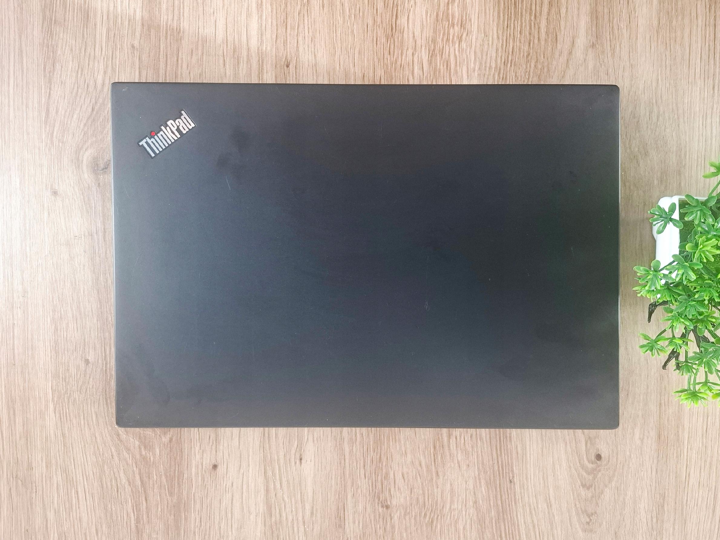 Zamknięta klapa laptopa ThinkPad widziana z góry, czarna matowa obudowa z widocznym logo, na drewnianym blacie.