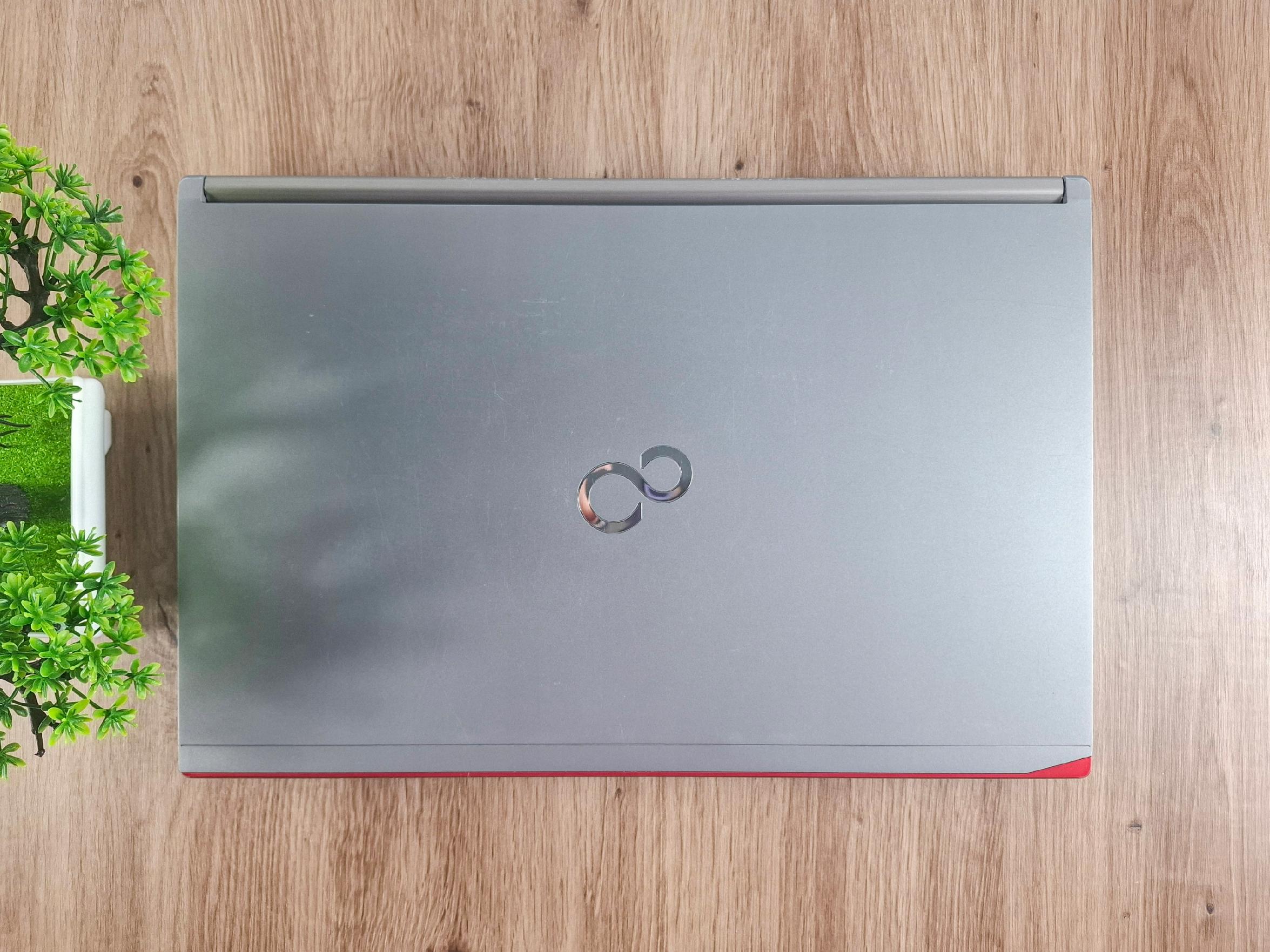 Zamknięta pokrywa laptopa Fujitsu z widocznym logo, ujęcie z góry, obudowa w kolorze srebrnym z widocznymi drobnymi rysami.