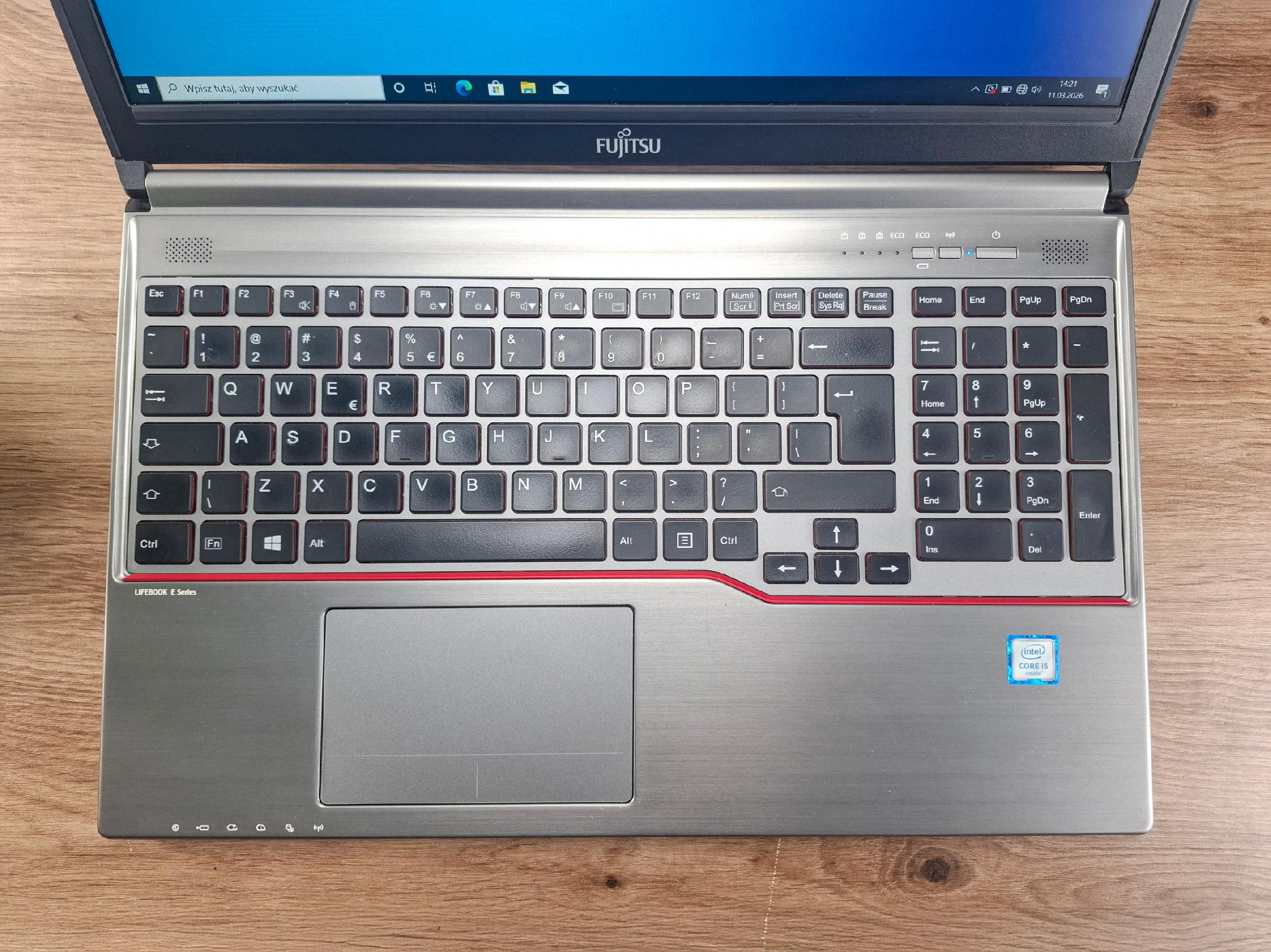 Otwarty laptop Fujitsu Lifebook widziany z góry, klawiatura z blokiem numerycznym i czerwonym akcentem, ekran włączony na pulpit Windows.