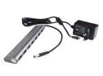 Aluminiowy hub USB i-tec z rzędem portów z przodu, podłączony kablem do czarnej ładowarki sieciowej.