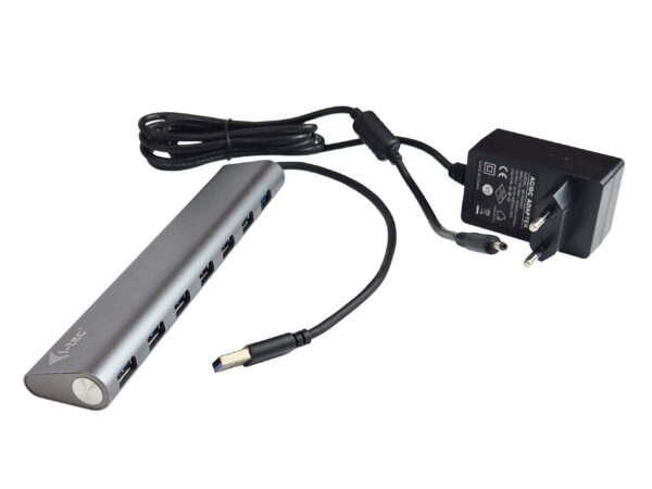 Aluminiowy hub USB i-tec z rzędem portów z przodu, podłączony kablem do czarnej ładowarki sieciowej.