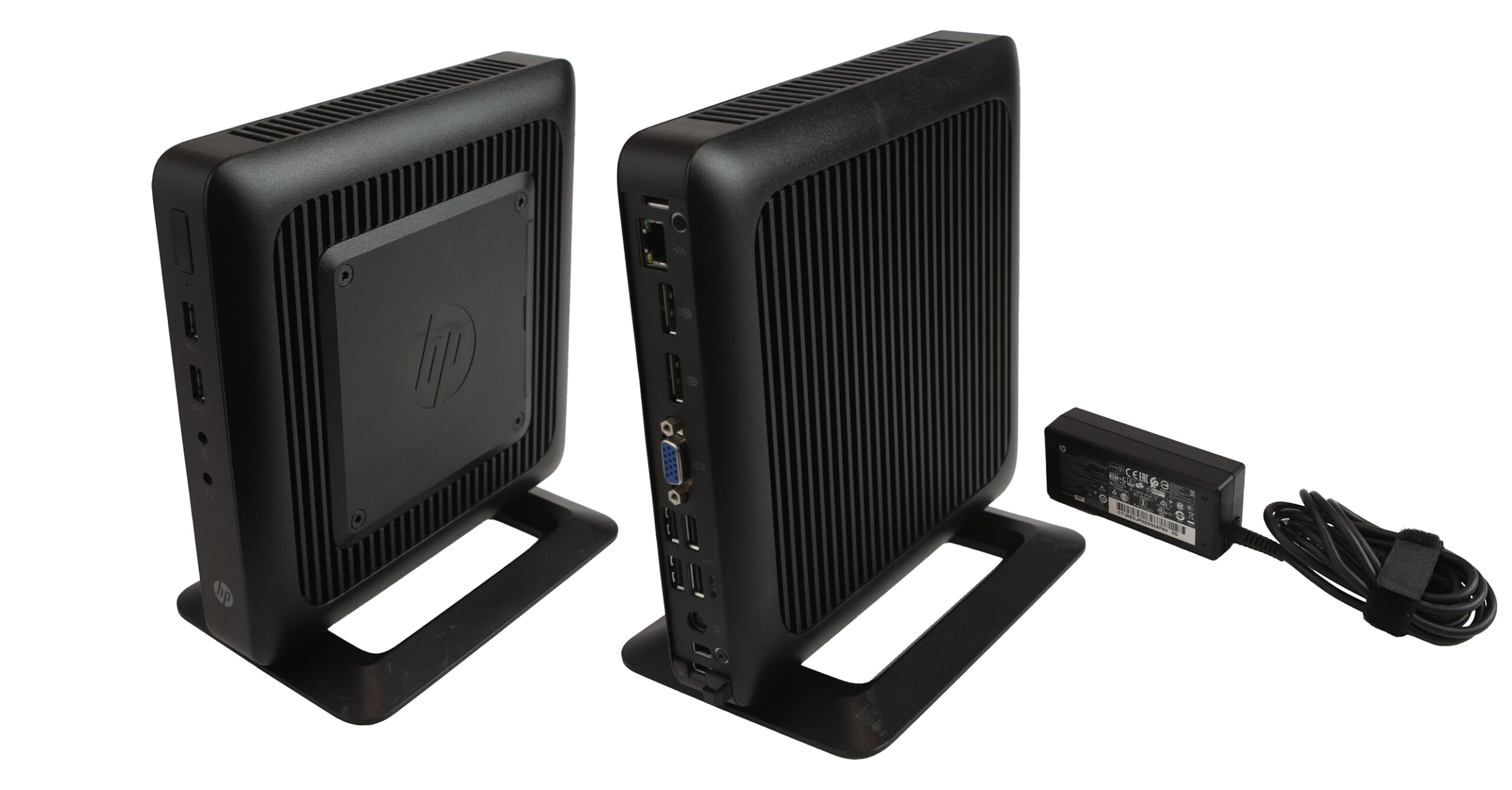 Dwa thin clienty HP t520 na podstawkach, widok z boku i z przodu, obok czarny zasilacz z kablem.
