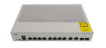 Przód switcha Cisco Catalyst z ośmioma portami RJ45, dwoma portami combo SFP i żółtą naklejką informacyjną z boku obudowy.