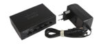 Switch Cisco SG110D-05 z przodu widoczne pięć portów RJ45, obok dołączony zasilacz sieciowy z przewodem