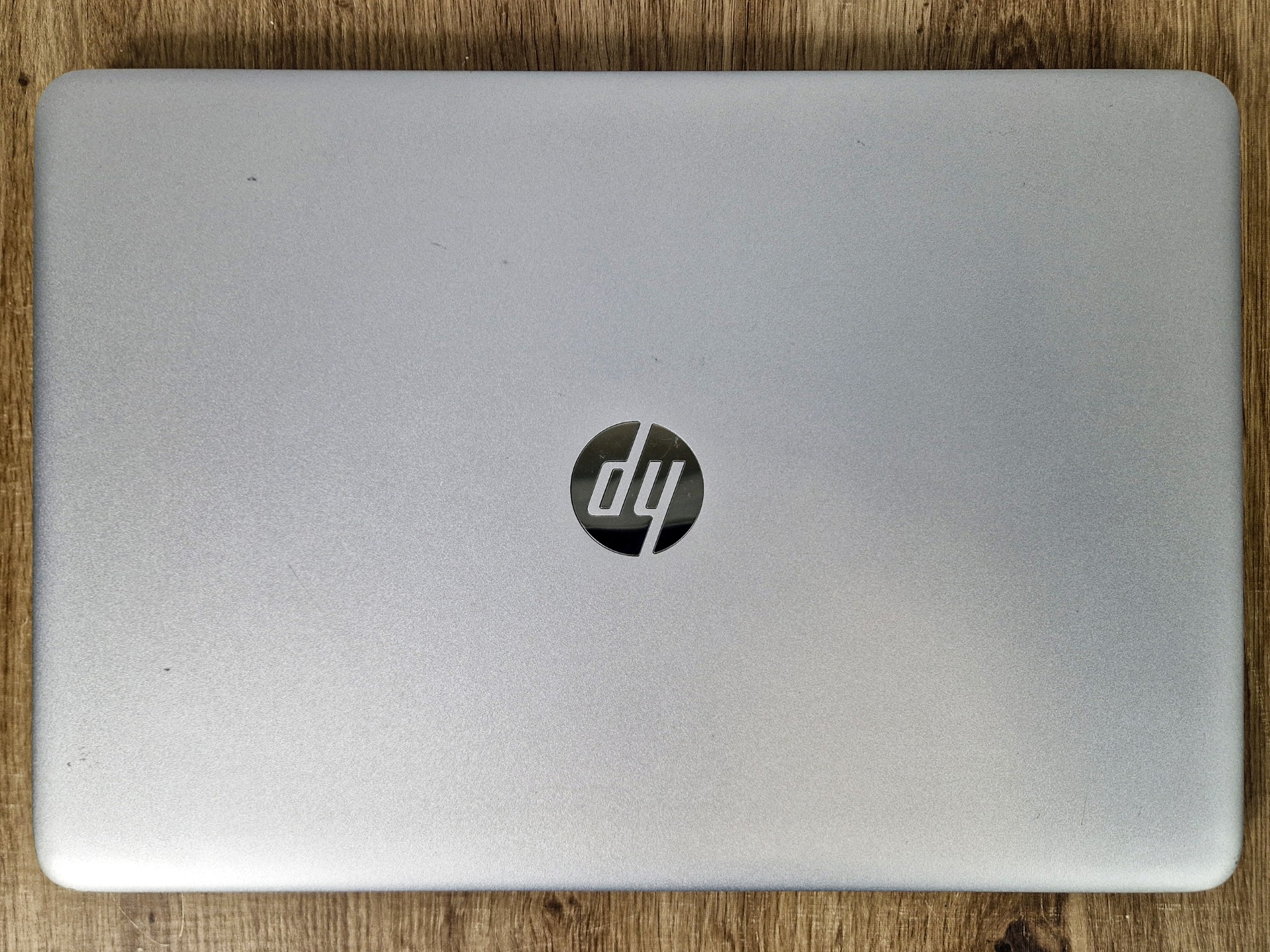 Zamknięta pokrywa laptopa HP widziana od góry z logo pośrodku, srebrna obudowa z lekkimi śladami użytkowania, na drewnianym blacie.