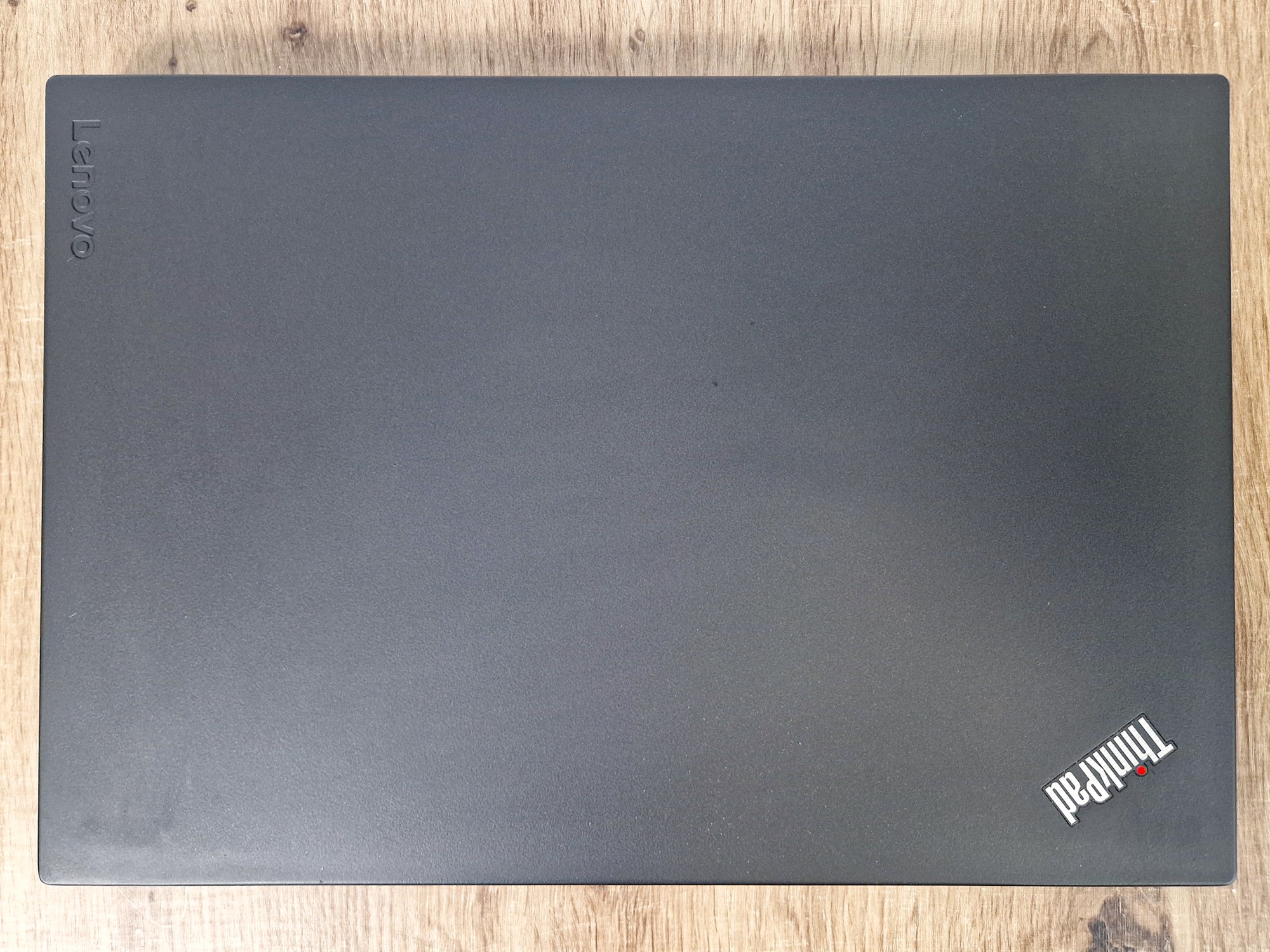 Zamknięta pokrywa laptopa ThinkPad widziana od tyłu, z logo Lenovo i ThinkPad, matowa czarna obudowa z drobnymi śladami użytkowania.
