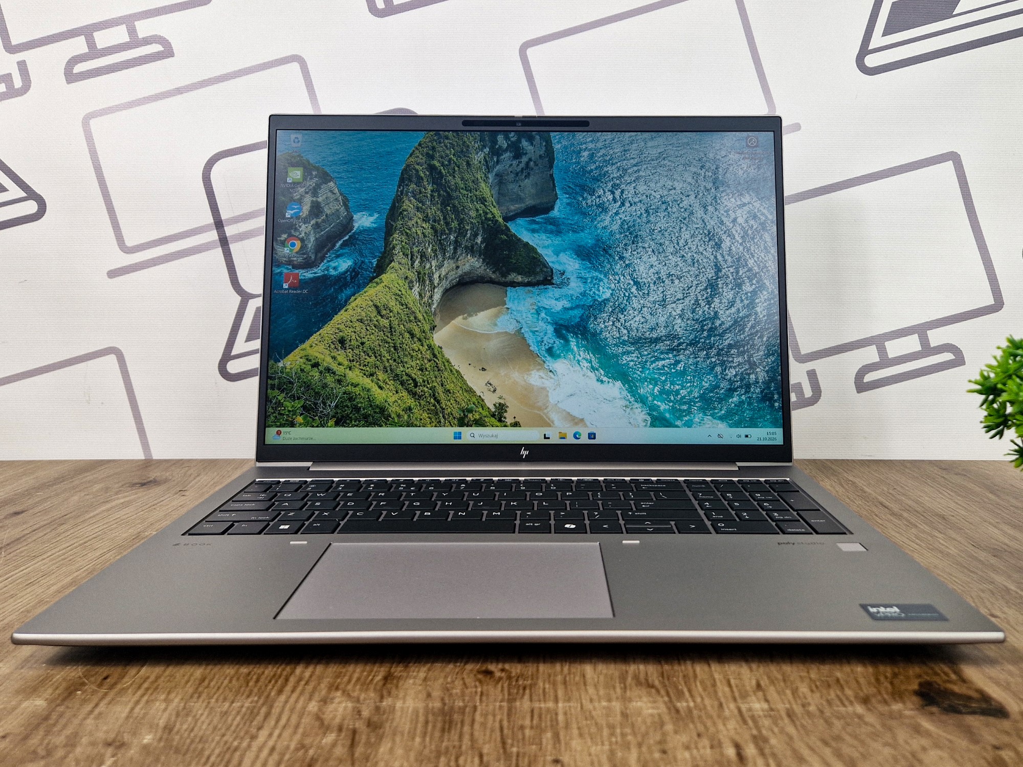 Otwarty laptop HP ZBook Firefly pod kątem z przodu, na ekranie zdjęcie tropikalnej wyspy, widoczna klawiatura i touchpad.
